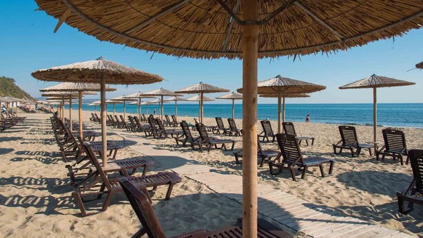 Une plage bordée de rangées de chaises longues et d’ombrelles en chaume.