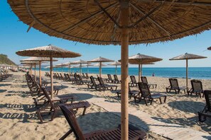 Une plage bordée de rangées de chaises longues et d’ombrelles en chaume.