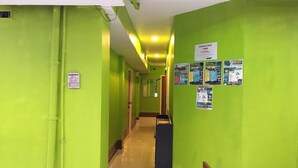 A hallway with green walls, a check-out time sign, and informational posters. - Lucky Guesthouse (Ko Phi Phi)