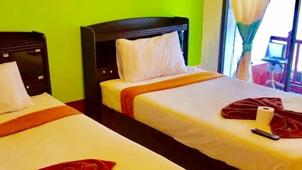 A hotel room with two beds, green walls, a framed picture on the wall, and a window with a green and white curtain. - Lucky Guesthouse (Ko Phi Phi)