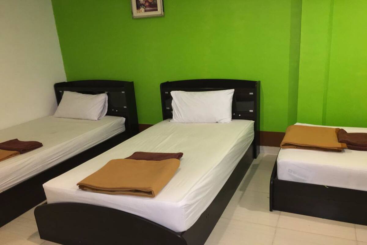 Ein Hotelzimmer mit zwei Einzelbetten, jeweils mit einer weißen Matratze und einer braunen Decke. Die Wände sind grün und der Boden ist mit Fliesen belegt.