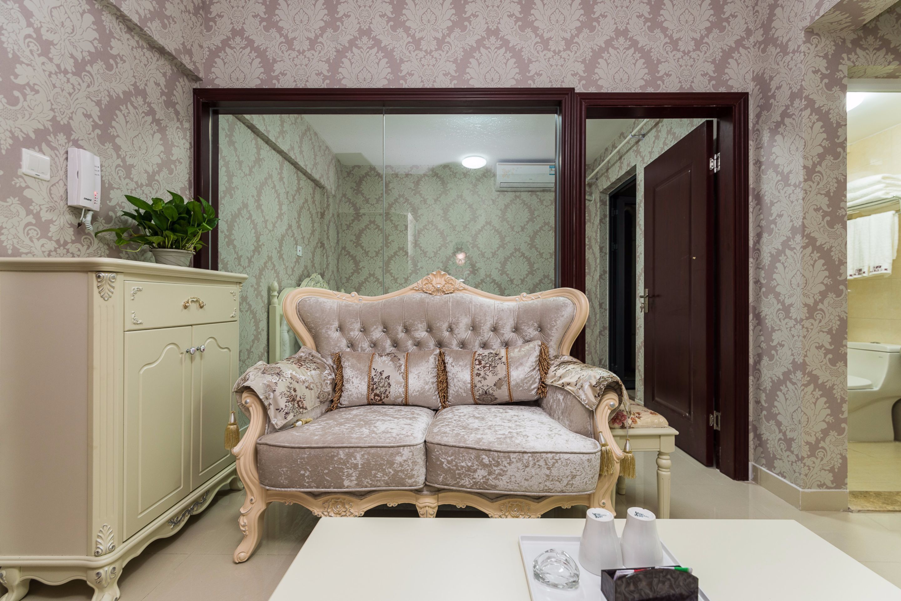 A room with a tufted sofa, a cabinet, and a table with a vase and a glass object.