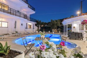 A swimming pool with lounge chairs and umbrellas, surrounded by a white building with balconies and outdoor seating. - Denise Studios & Apartments (Zakynthos)