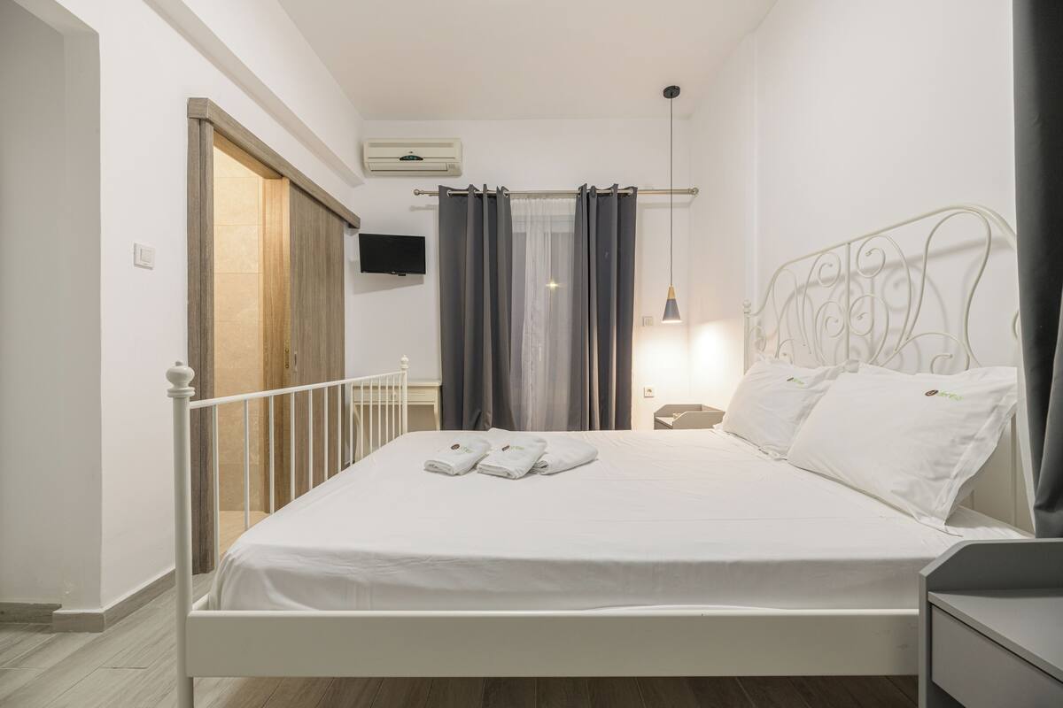 A neatly made bed with white linens and towels, a white metal headboard, and a bedside table with a lamp.