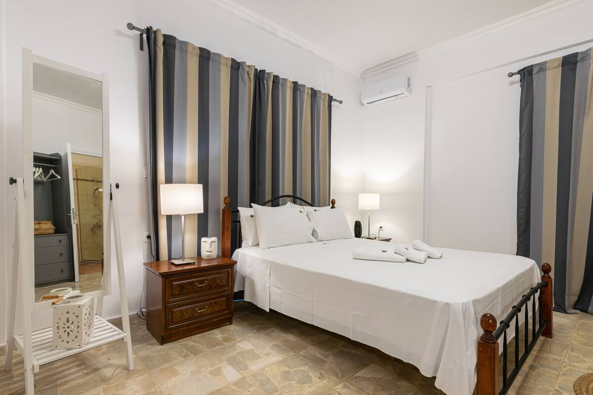 A bedroom with a bed, two bedside tables, a nightstand, a mirror, and a wardrobe.