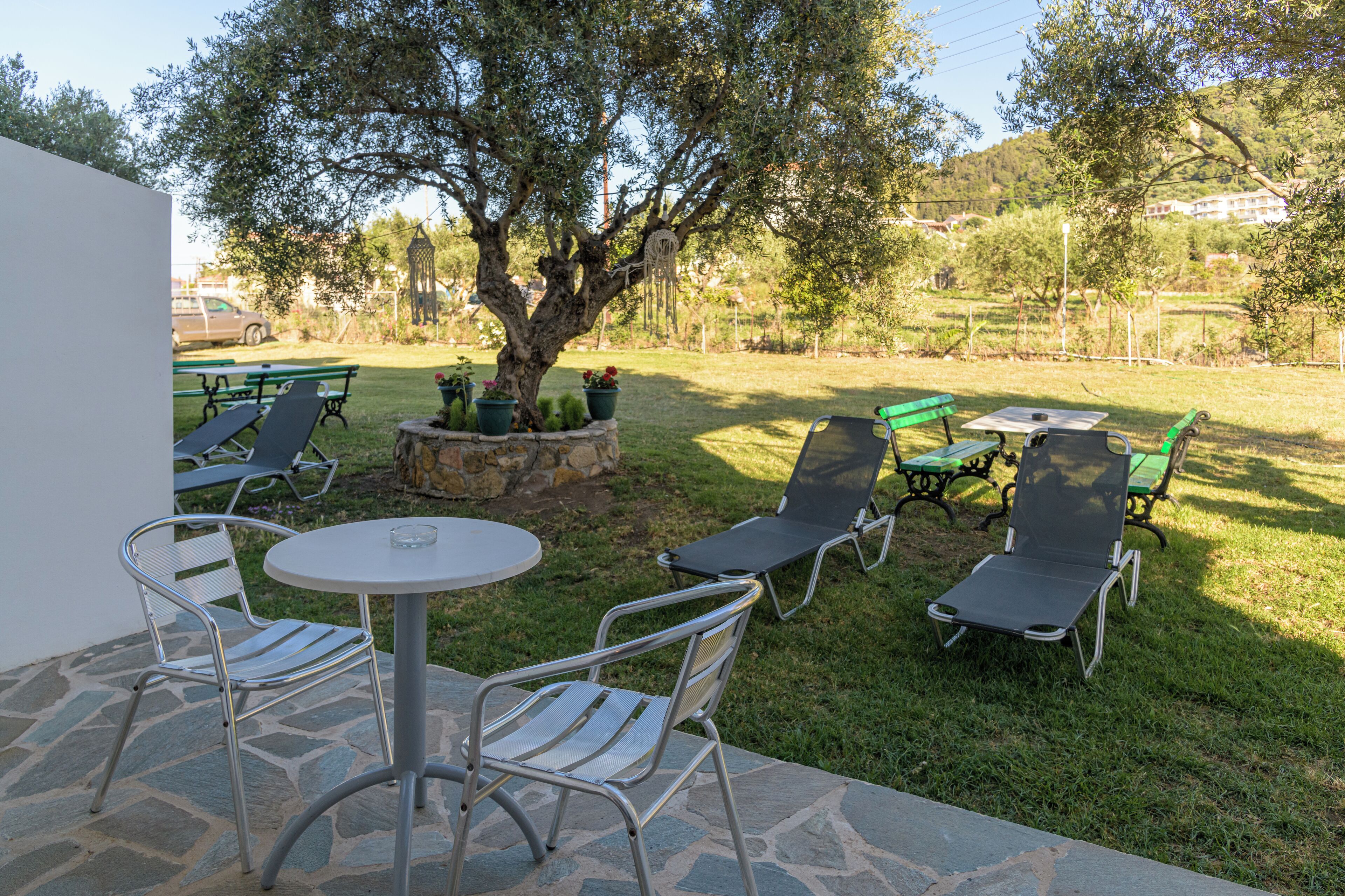 An outdoor patio with a stone table and chairs, surrounded by a grassy area with a tree and benches.
