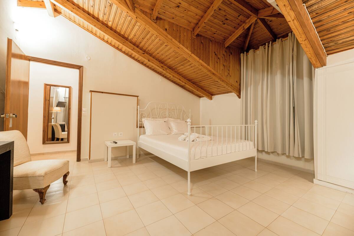 A bedroom with a wooden ceiling, a white bed, a chair, a nightstand, and a wardrobe.