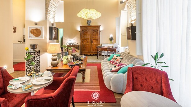 A cozy living room with a fireplace, red upholstered chairs, a wooden dining table, and a large arched doorway.