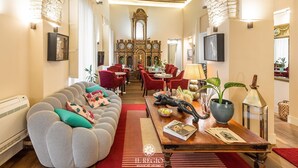 A spacious living room with a high arched brick ceiling, a wooden coffee table, red upholstered chairs, and a grey sofa with patterned cushions.