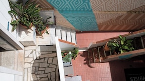 A multi-level building with potted plants on balconies, a patterned ceiling, and a brick wall.