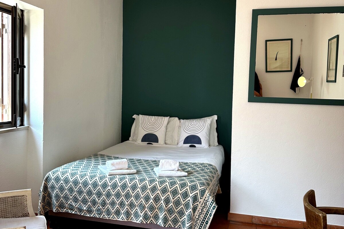 A room with a bed, a chair, a hanging light fixture, and a wall-mounted picture frame.