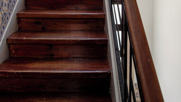A wooden staircase with a metal handrail, leading to a landing with a potted plant.