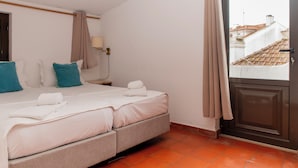 A hotel room with a bed, a nightstand, a lamp, and a view of buildings through a door.
