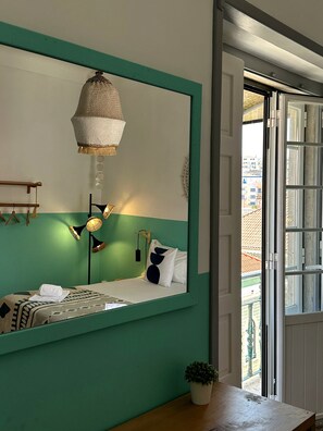 A room with a bed, a hanging lamp, a potted plant, and a view of buildings through a window.