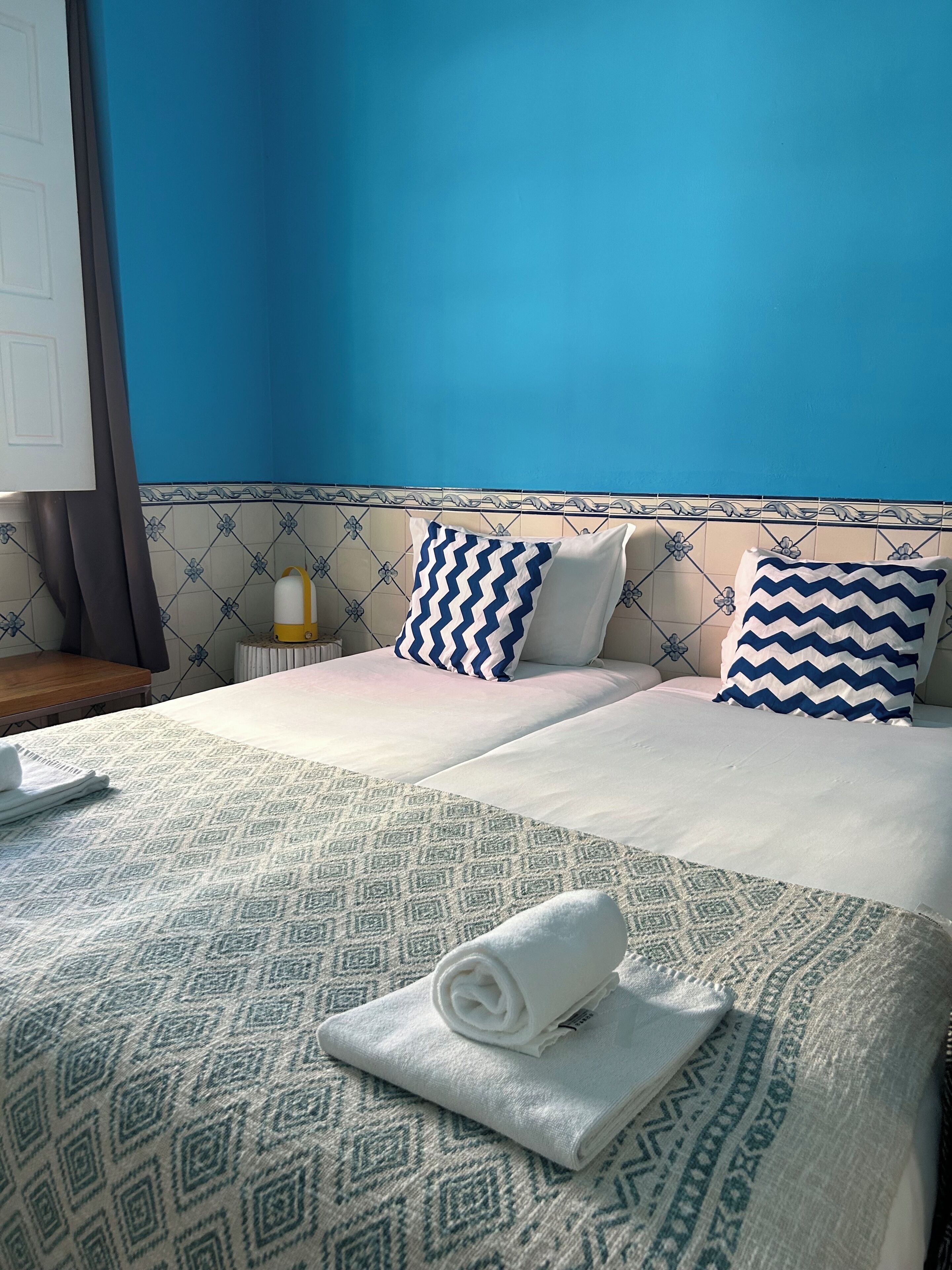 A hotel room with a bed, two pillows, a bedside table, and a towel.
