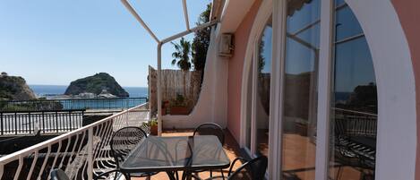 A balcony with a table and chairs, a railing, and a view of the sea and a rocky island.