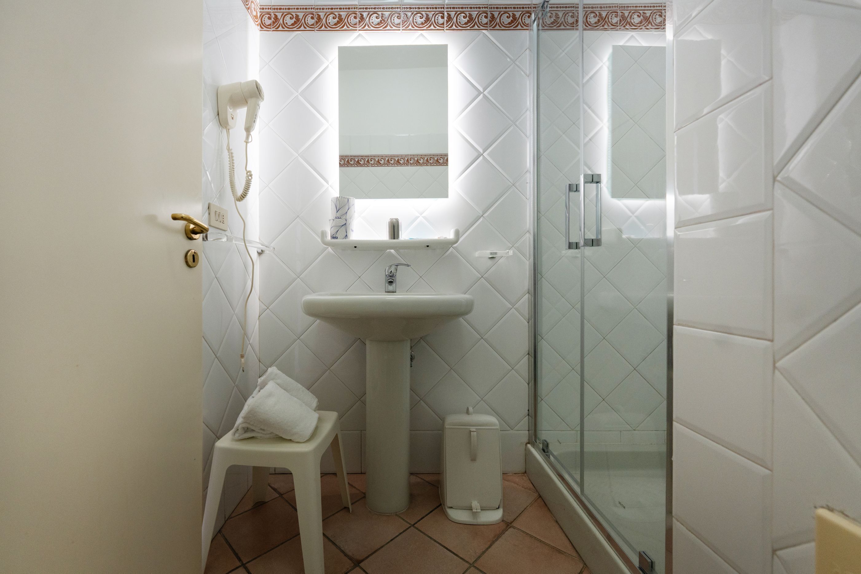 A bathroom with a pedestal sink, a mirror, a towel rack, a glass shower enclosure, and a toilet.
