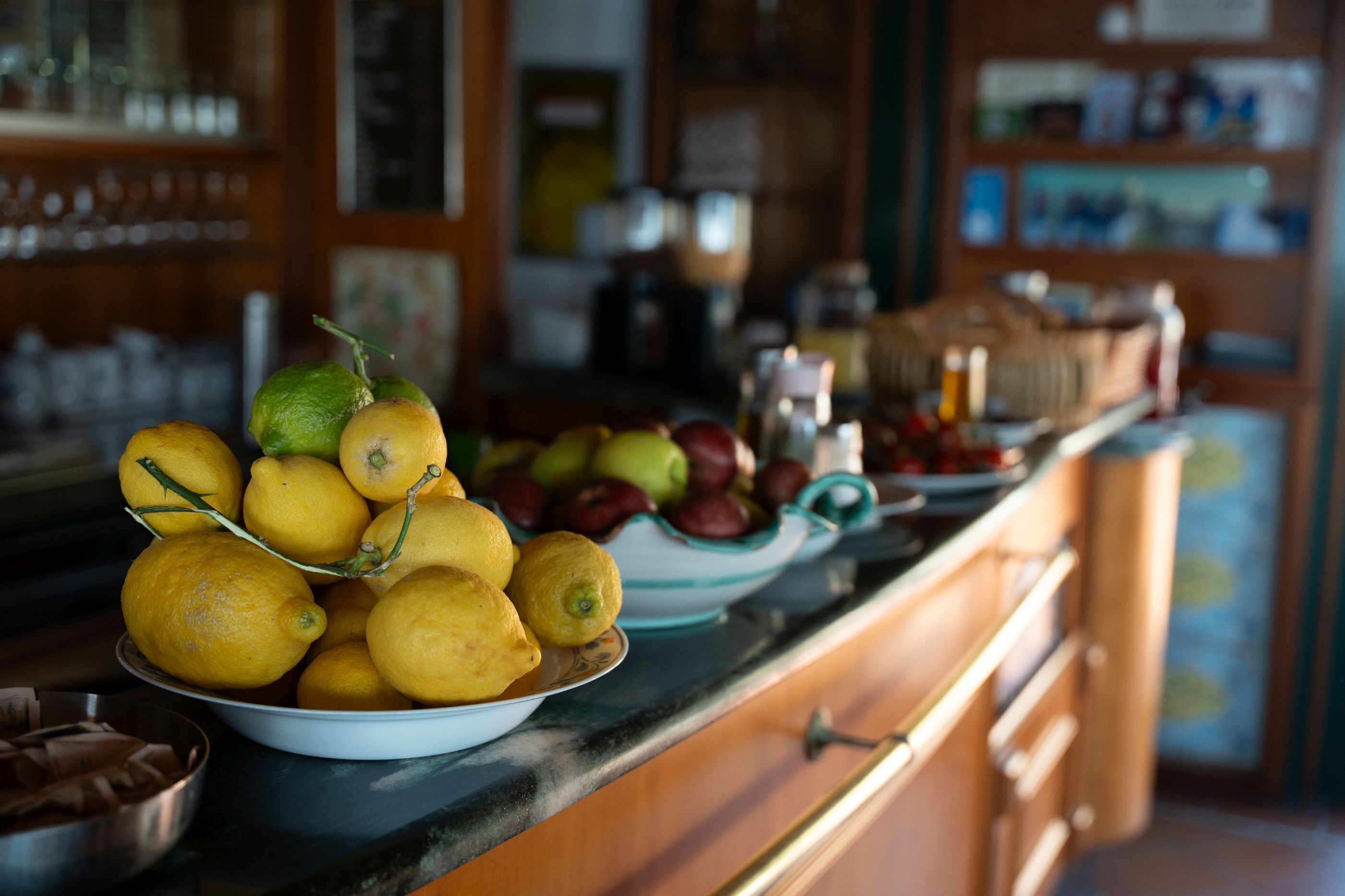 A kitchen counter with bowls of lemons and apples, a sink, and cabinets.