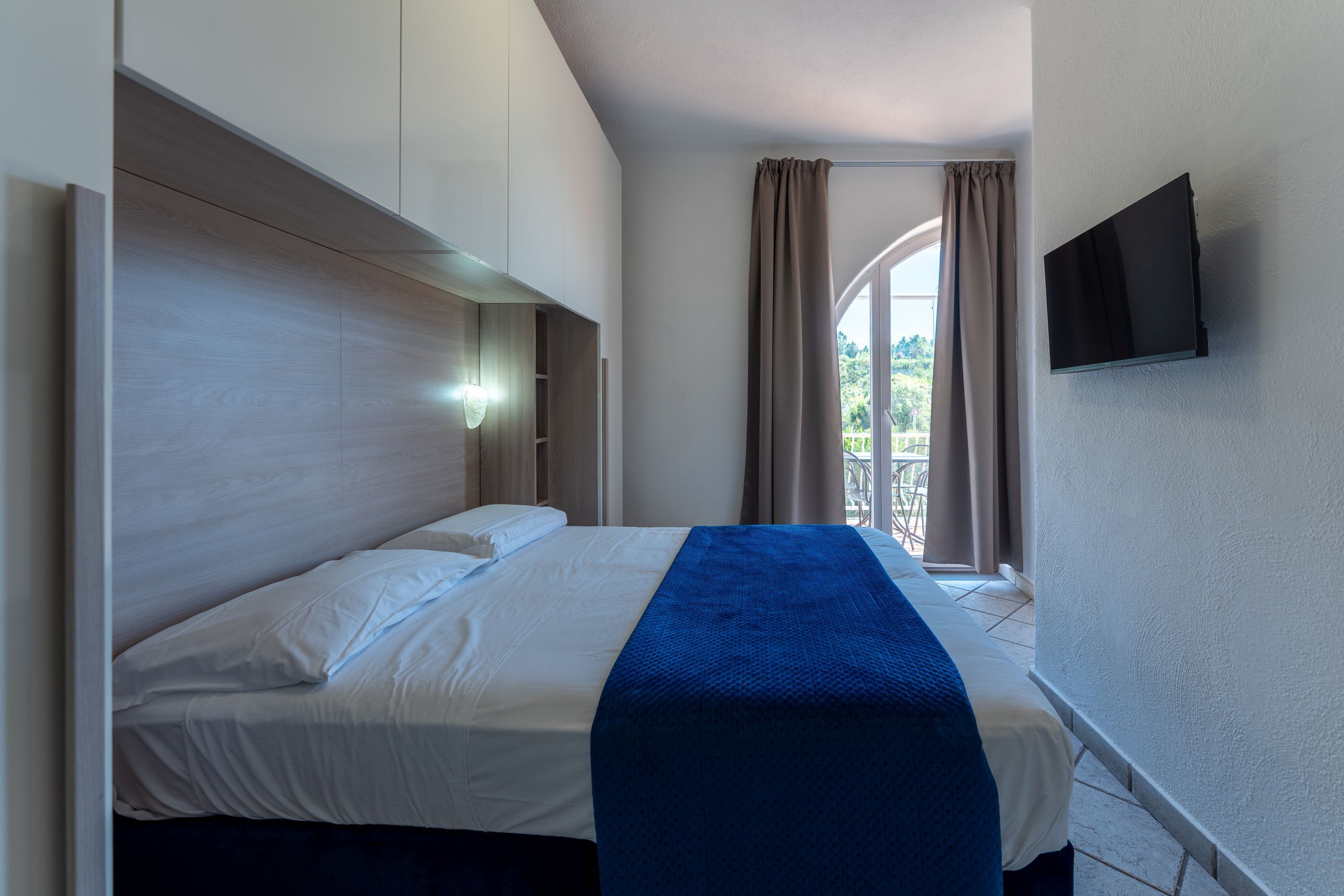 A hotel room with a bed, a TV mounted on the wall, and a window with curtains.