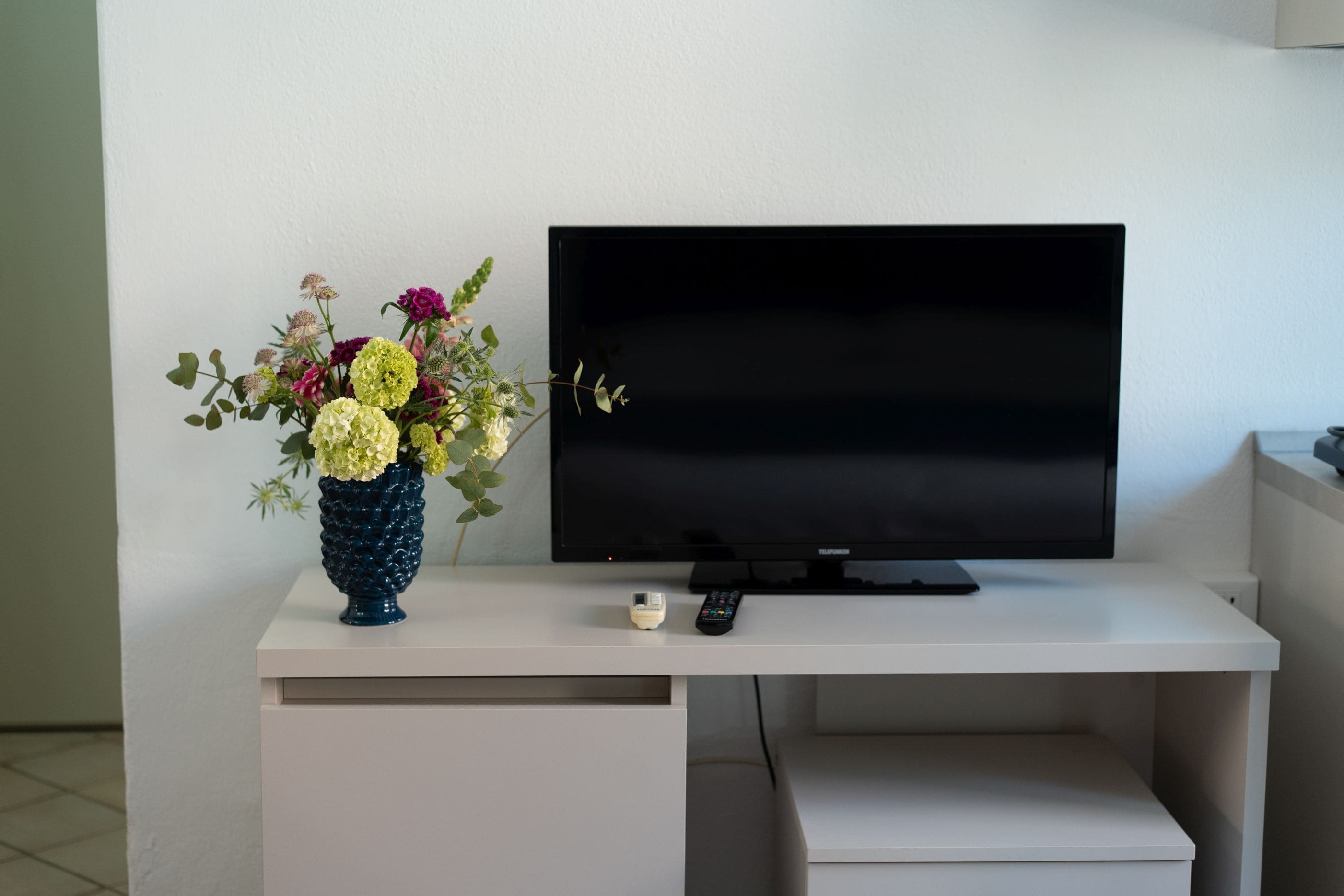 Un televisor de pantalla plana sobre un escriptori blanc amb un ram de flors.