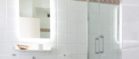 A bathroom with a sink, mirror, shower, and a towel on a bench.