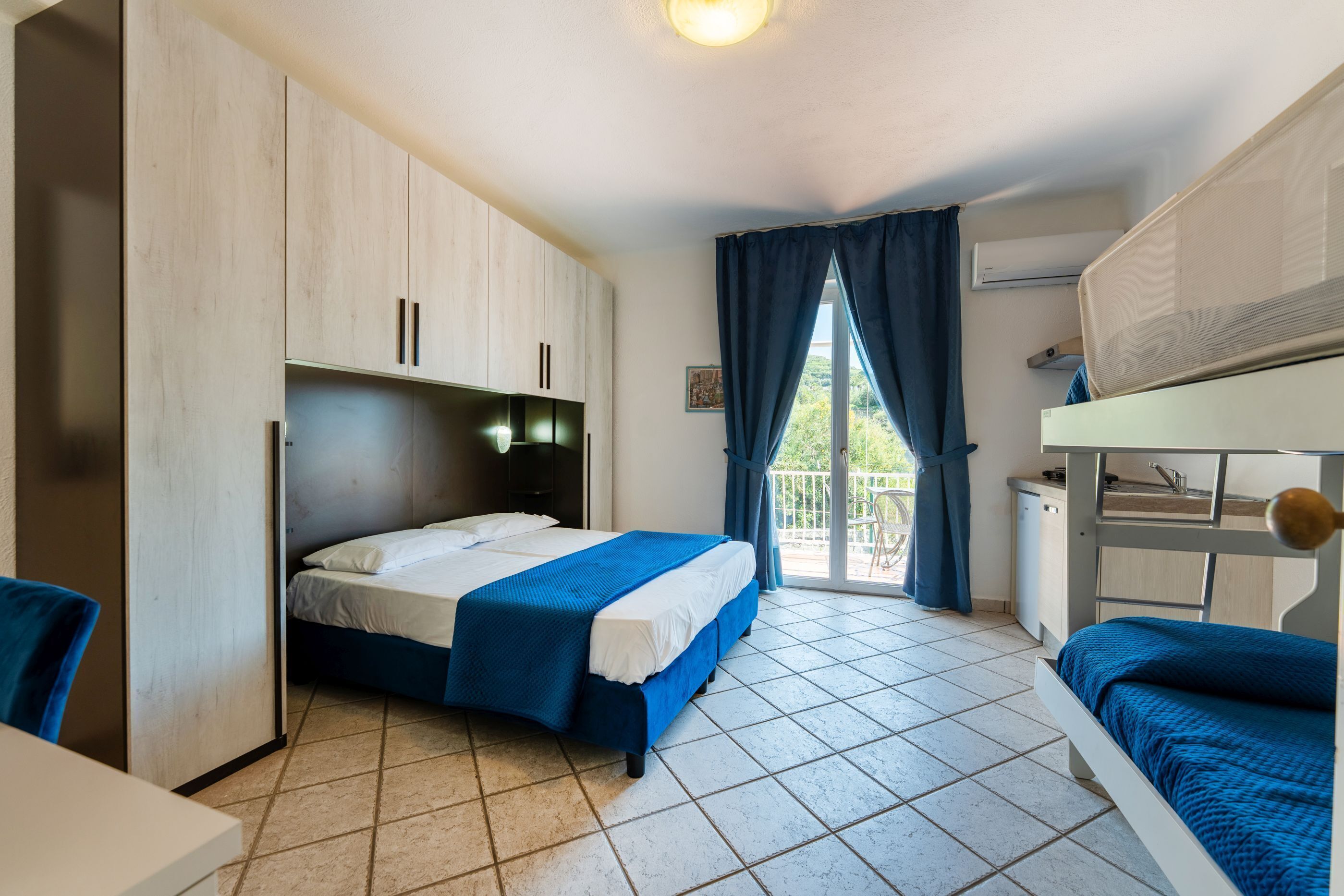 Une chambre avec un lit, un bureau, un lit superposé et une fenêtre avec des rideaux.