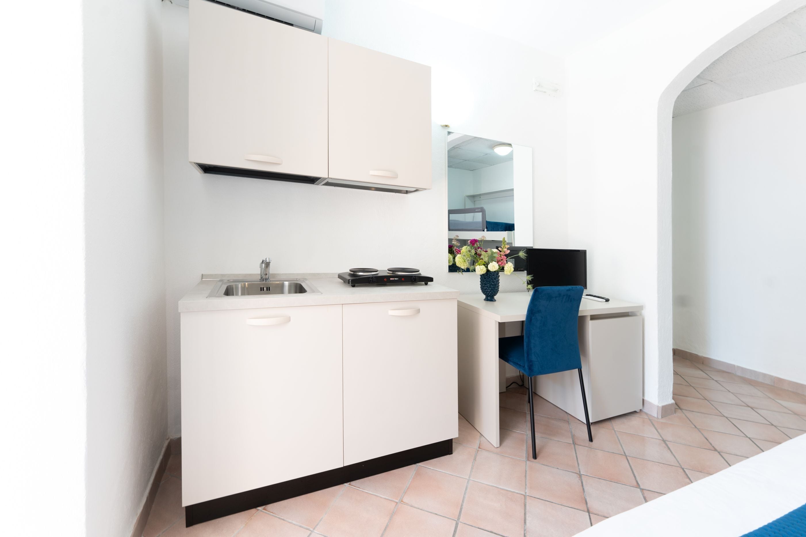 A compact kitchen with a sink, stove, and a chair.