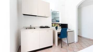 A compact kitchen with a sink, stove, and a chair.