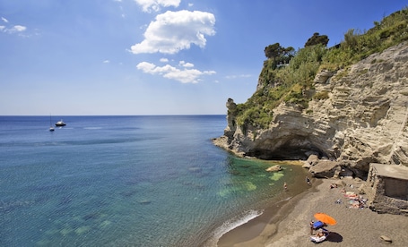 A beach with clear water, a rocky cliff, and a boat in the distance.