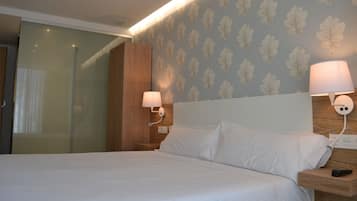 Une chambre d’hôtel avec un lit, deux lampes de chevet, une tête de lit en bois et un papier peint à motifs.