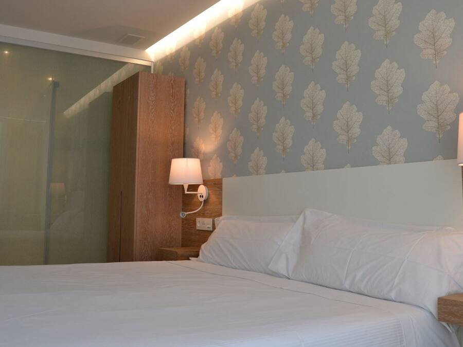 Une chambre d’hôtel avec un lit, deux lampes de chevet, une tête de lit en bois et un papier peint à motifs.