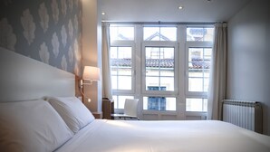 Habitación de hotel con una cama grande, una silla, un escritorio y una ventana con vista a edificios.