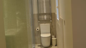 Un baño pequeño con cabina de ducha de vidrio, un inodoro y un cubo de basura.