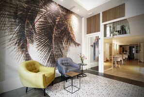 Un hall d’entrée moderne agrémenté d’une grande fresque représentant des feuilles de palmier, d’un fauteuil jaune, d’un fauteuil gris et d’une petite table ornée de fleurs.