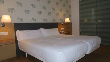 Habitación de hotel con una cama grande, dos lámparas de noche, una mesita de noche y una pared con diseños de elefantes.