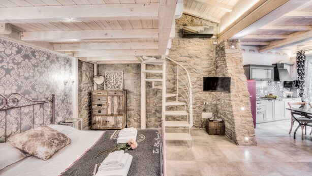 A bedroom with a bed, a bedside table with towels, a dresser, a stone wall, a wooden ceiling, and a staircase leading to an upper level. - Giglio Apartments by Mmega (Florence)