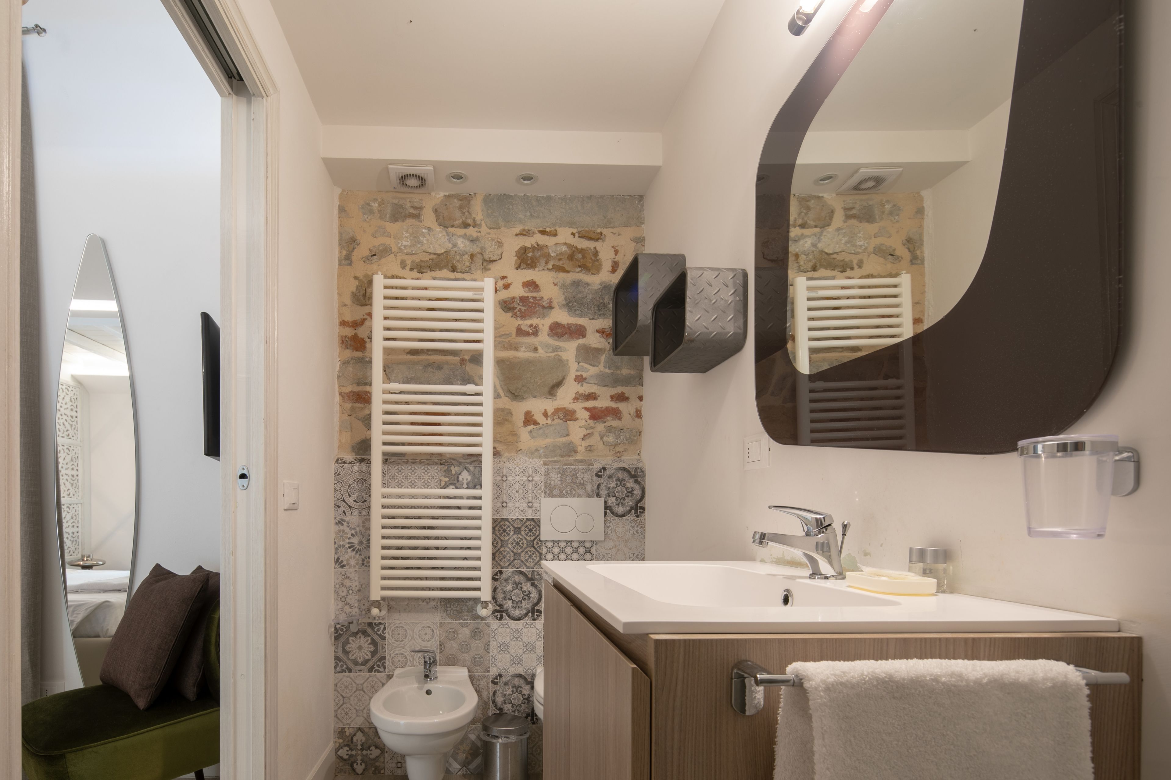 A bathroom with a stone wall, a sink, a mirror, and a towel rack.