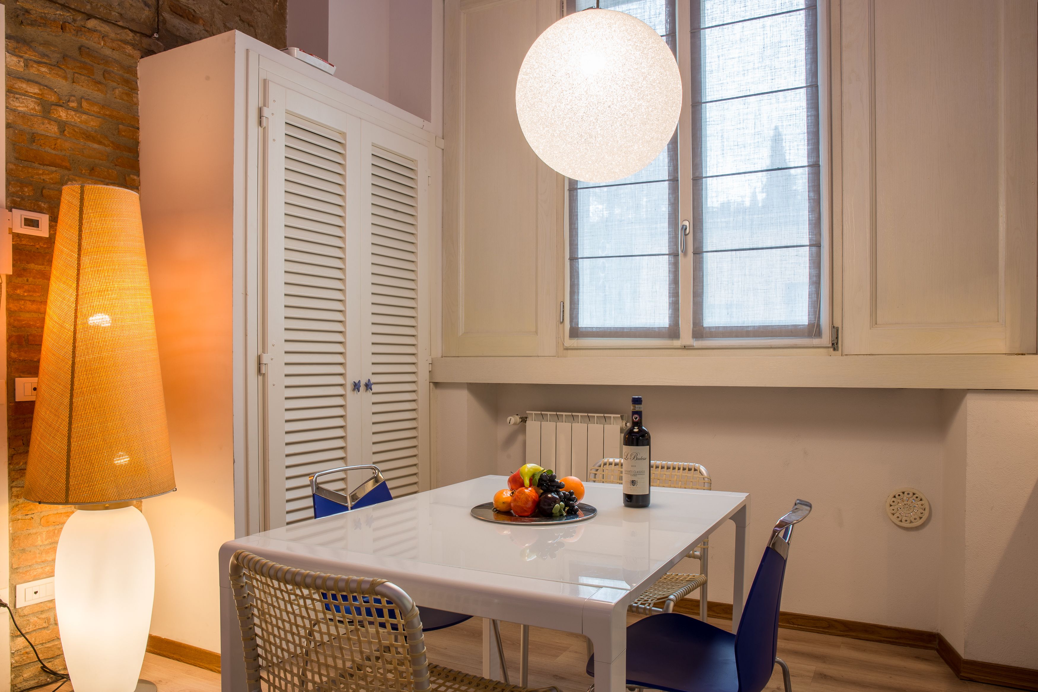 A dining area with a table set for two, a fruit plate, a bottle of wine, and a hanging light fixture.