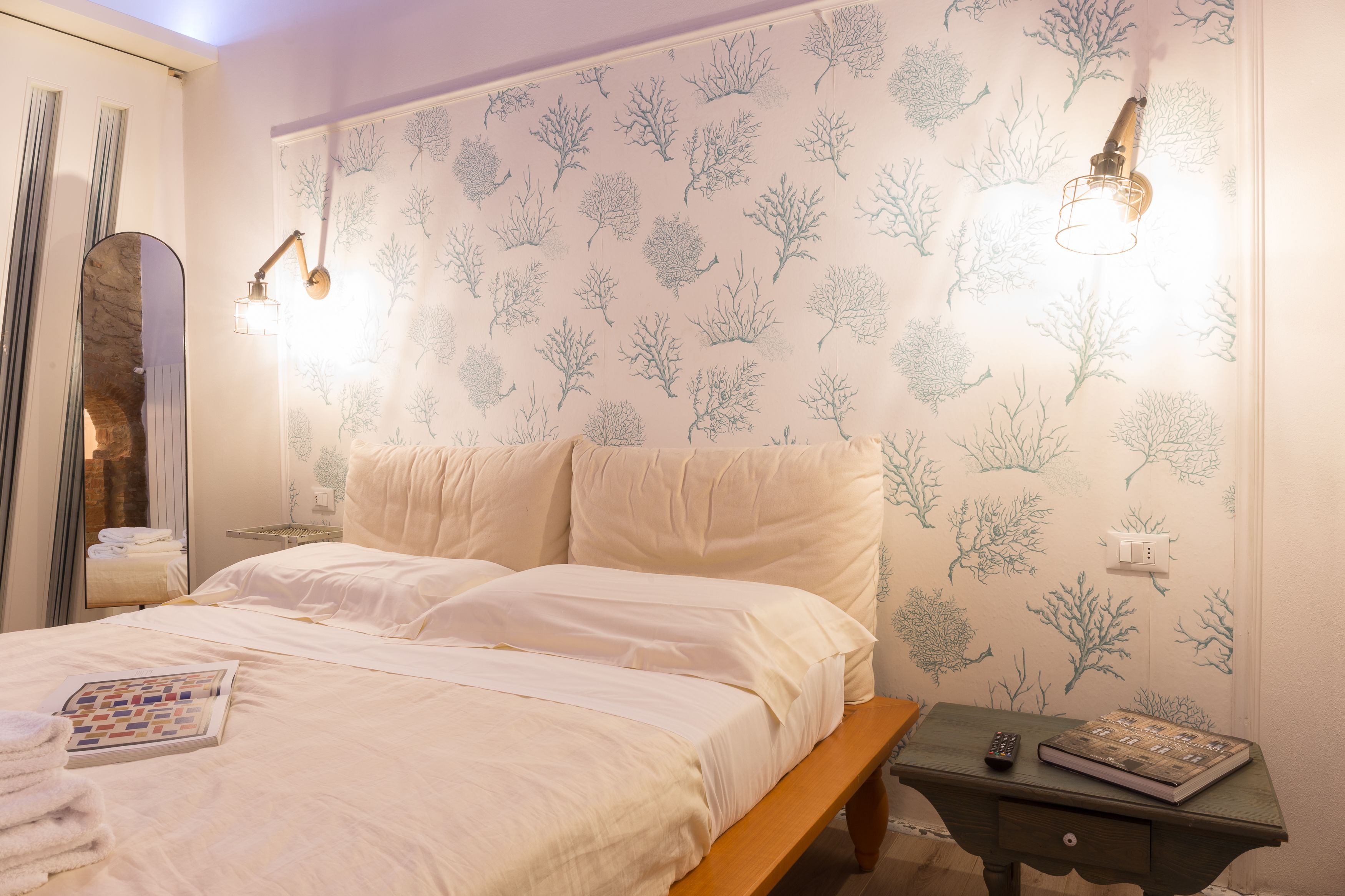 Quarto com cama, mesa de cabeceira, espelho e parede com padrão de árvore.