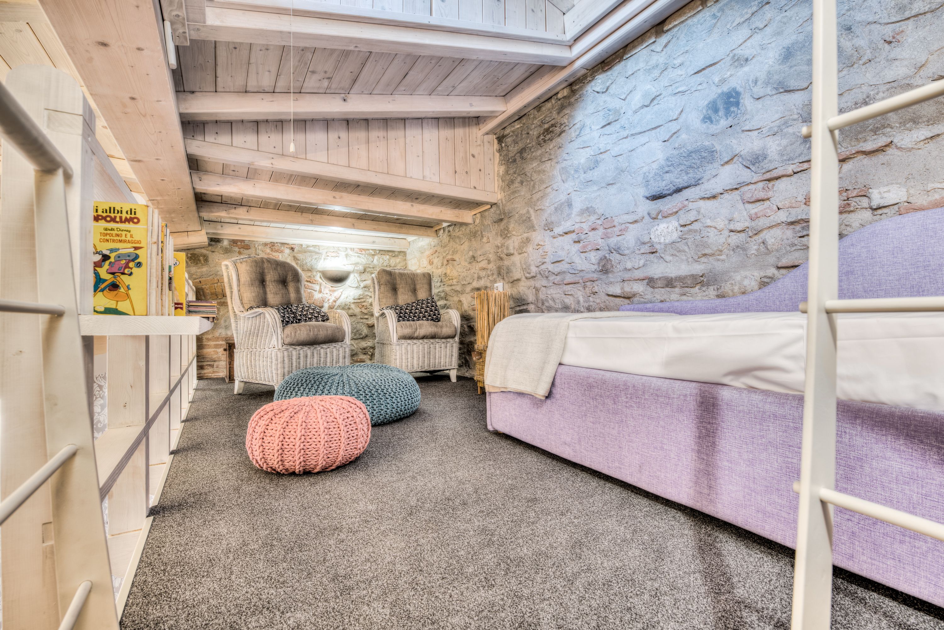 A cozy room with a bunk bed, two wicker chairs, a stone wall, and a wooden ceiling.