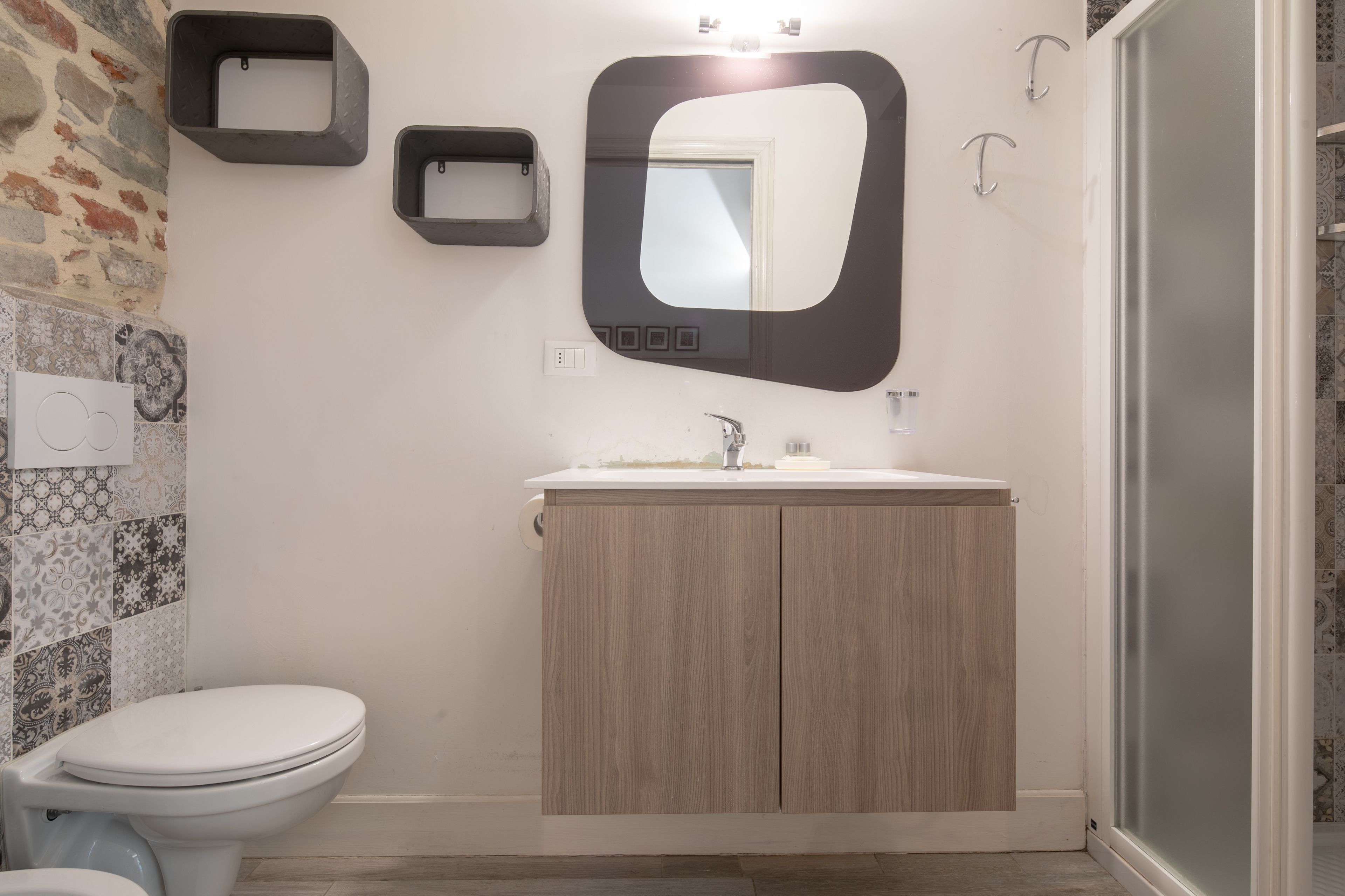 A bathroom with a toilet, sink, and mirror. There are decorative tiles on the wall and a shower area.