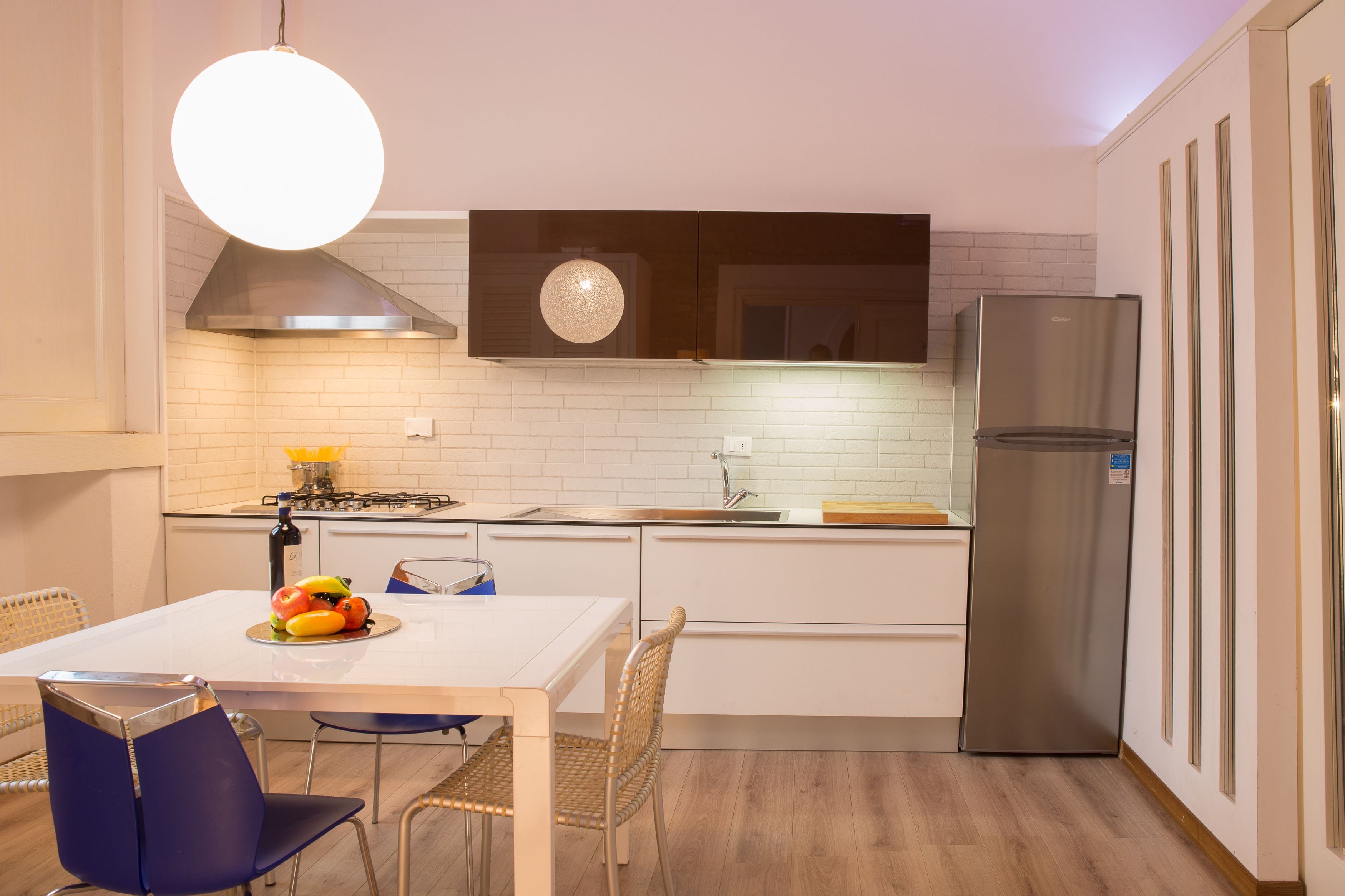 Een moderne keuken met witte kasten, een roestvrijstalen koelkast, een gasfornuis en een eethoek met een tafel en stoelen.