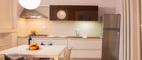 Een moderne keuken met witte kasten, een roestvrijstalen koelkast, een gasfornuis en een eethoek met een tafel en stoelen.