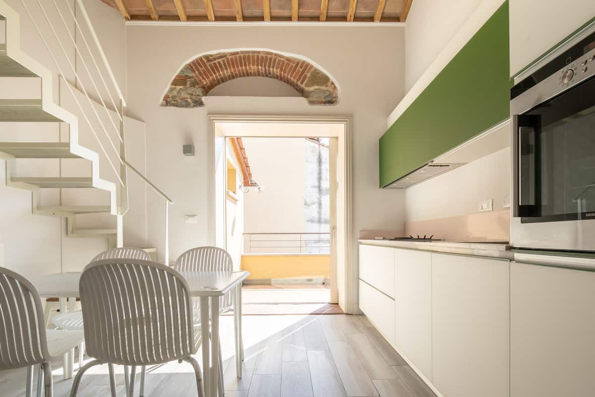 A modern kitchen with white cabinetry, a built-in oven, and a dining area with a table and chairs.