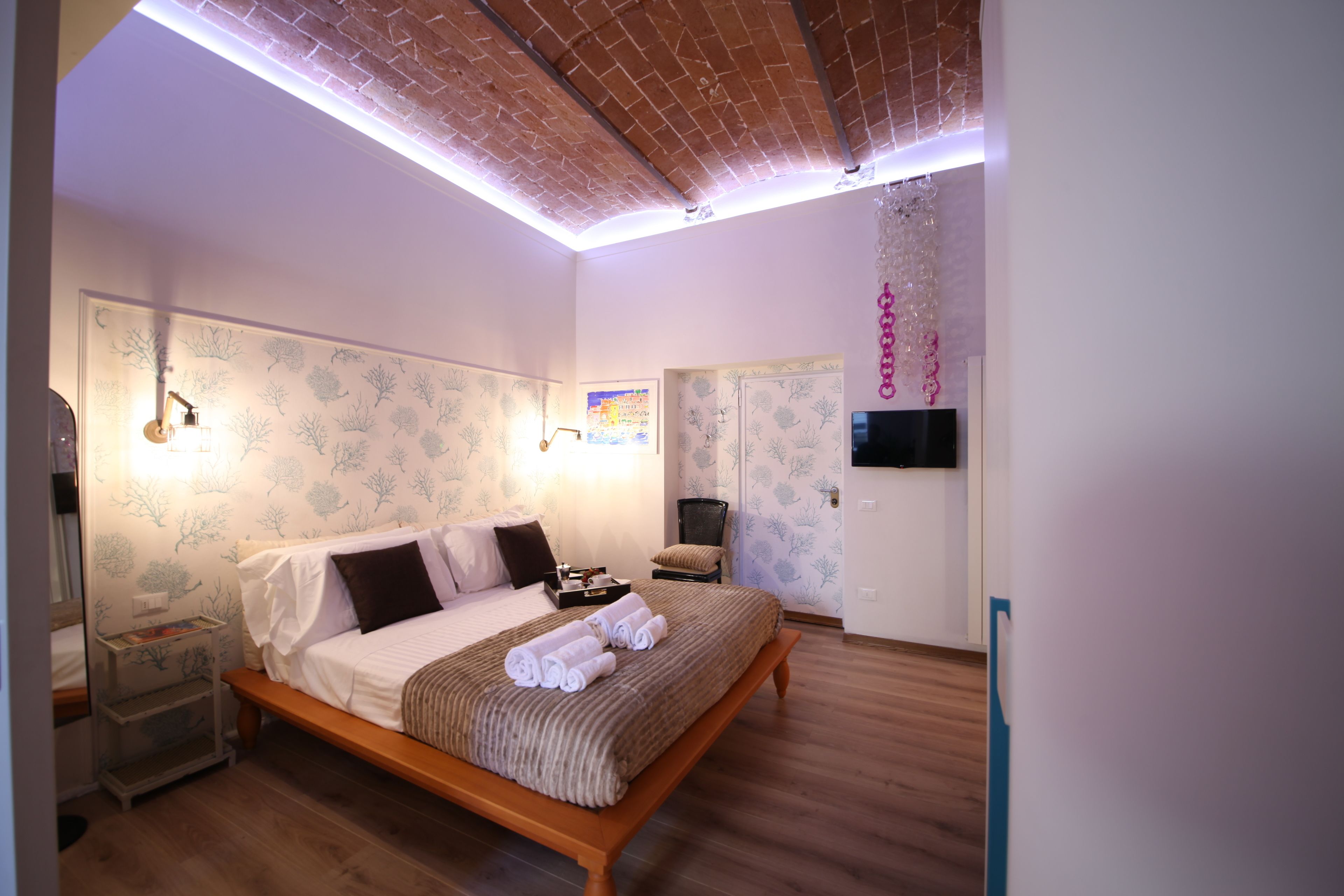 A bedroom with a wooden bed, a nightstand, a wall-mounted TV, and a ceiling with exposed beams.