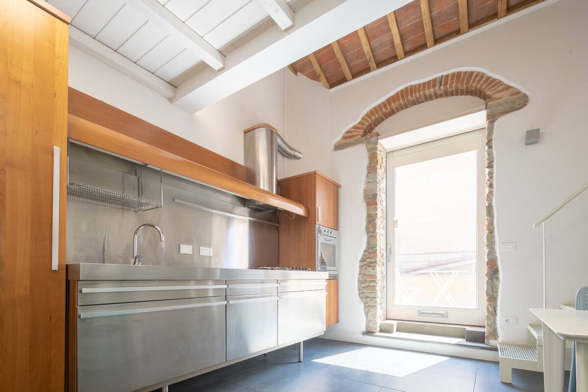 A modern kitchen with stainless steel appliances, wooden cabinets, and a stone archway leading to a balcony.