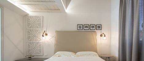 Een net opgemaakt bed met handdoeken, een nachtkastje met een lamp, en lijstjes met foto's aan de muur.