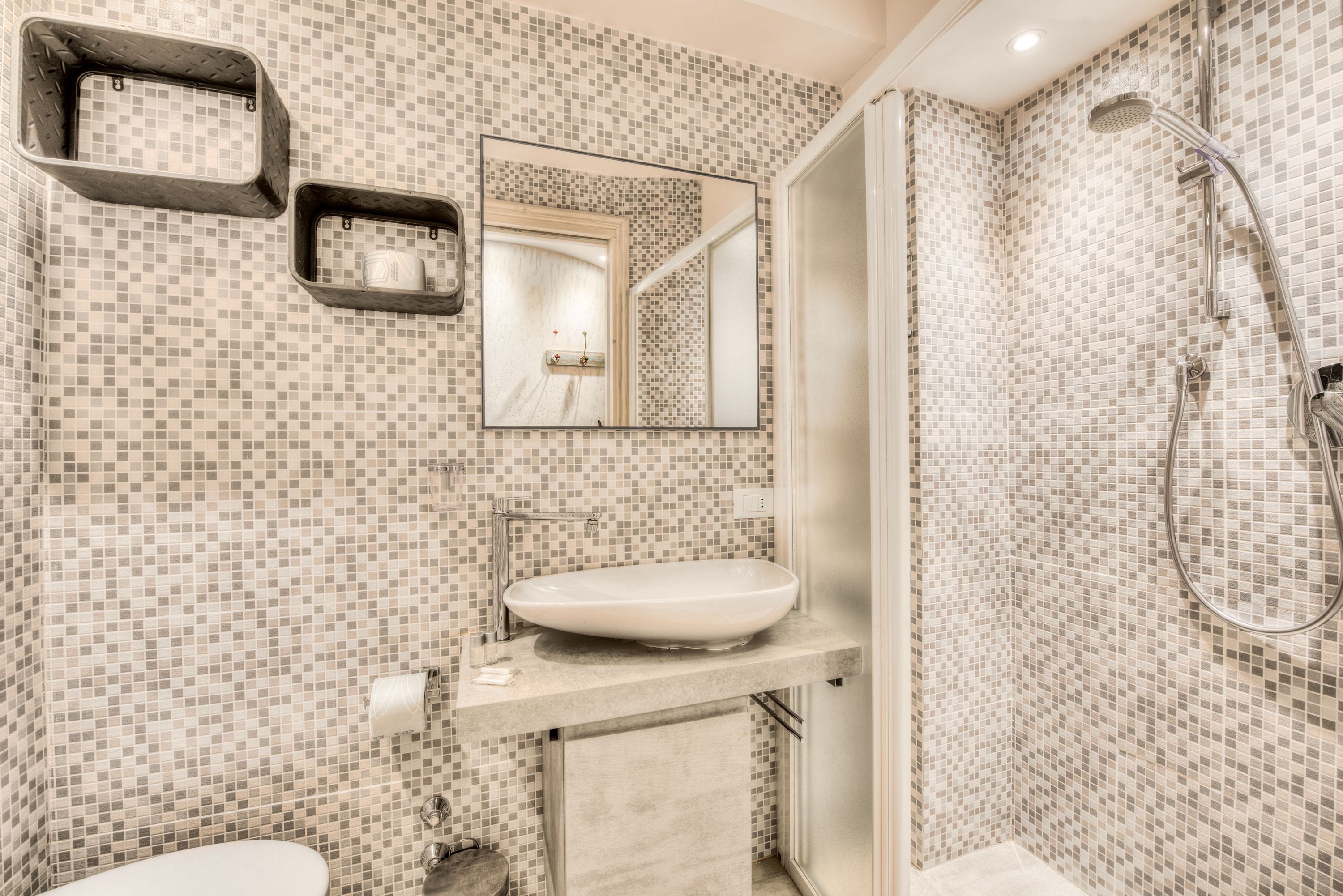 A bathroom with a tiled mosaic floor, a white sink, a mirror, and a shower area.