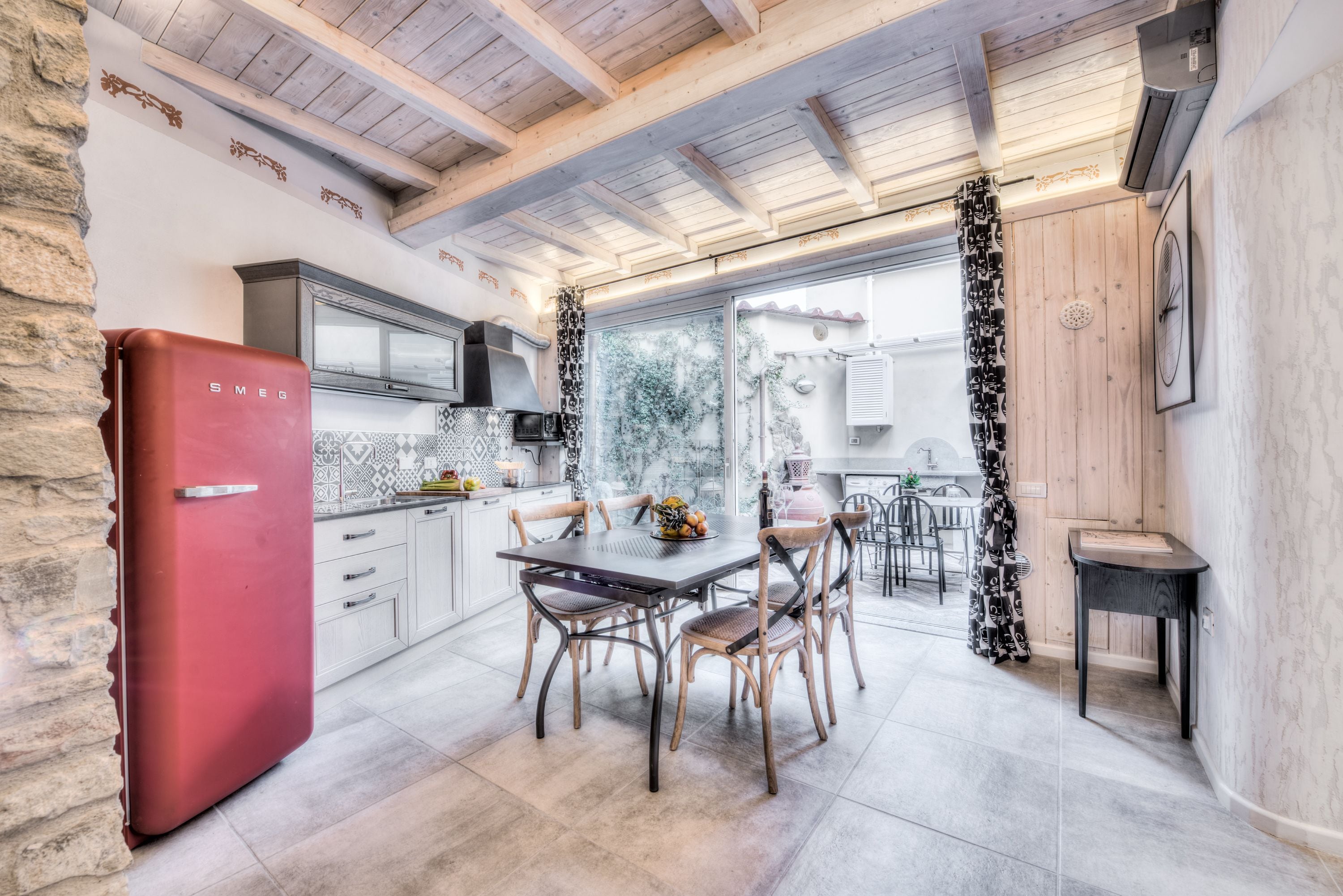 Une cuisine avec un réfrigérateur rouge, des poutres en bois au plafond et un coin repas comprenant des chaises et une table.