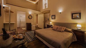 Un dormitorio espacioso con una cama grande, una mesita de noche con lámpara, una mesita auxiliar y techo de madera, con vista al baño.
